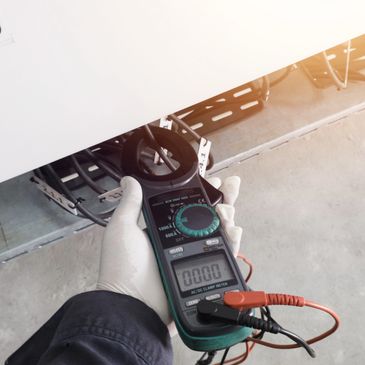 Hand holding a clamp meter measuring electrical current in cables.