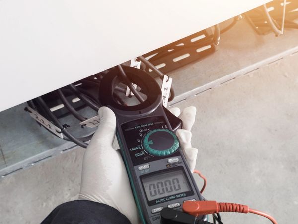 Hand holding a clamp meter measuring electrical current in cables.