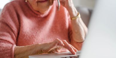 Elderly woman using laptop and talking on phone.