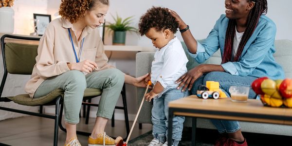 Two women and a toddler playing with toys in a cozy living room.