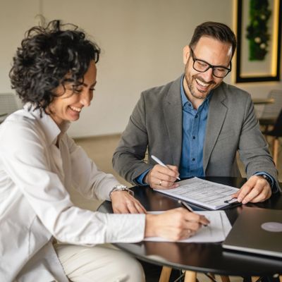 Two colleagues happily signing documents at a table.