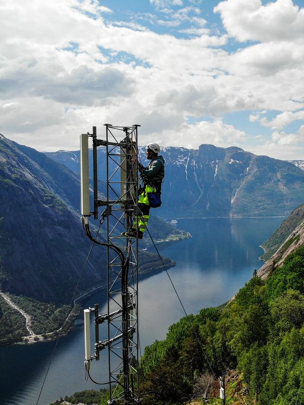 Technician repairing antenna tower by mountainous river.