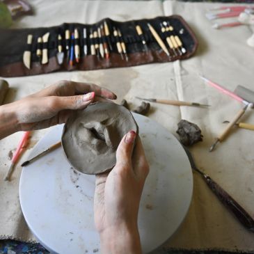 Hands sculpting clay on a pottery wheel with tools in the background.
