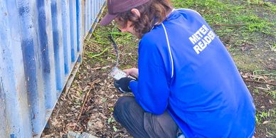 Person in blue reads a meter near a container outdoors.