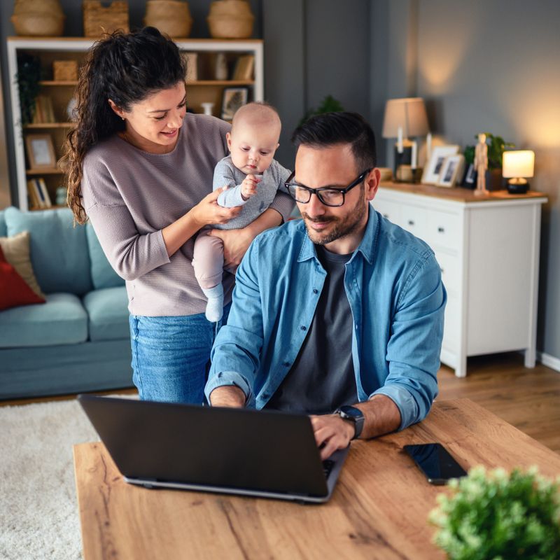 Family with a baby at home, Father using a laptop. Father is trying to work from home.