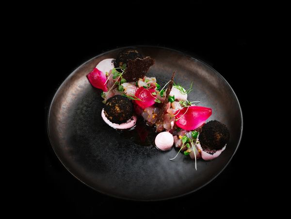 Elegant tartare dish with vibrant pink accents and dark crispy spheres on a black plate.