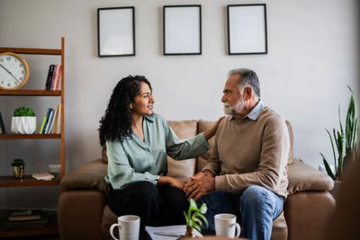 Woman comforting an elderly man on a couch at home.