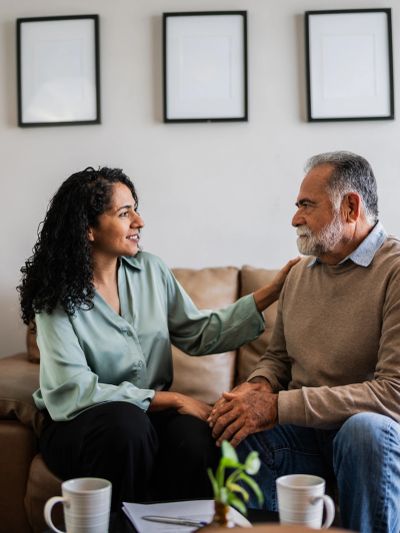 Woman comforting elderly man on couch.