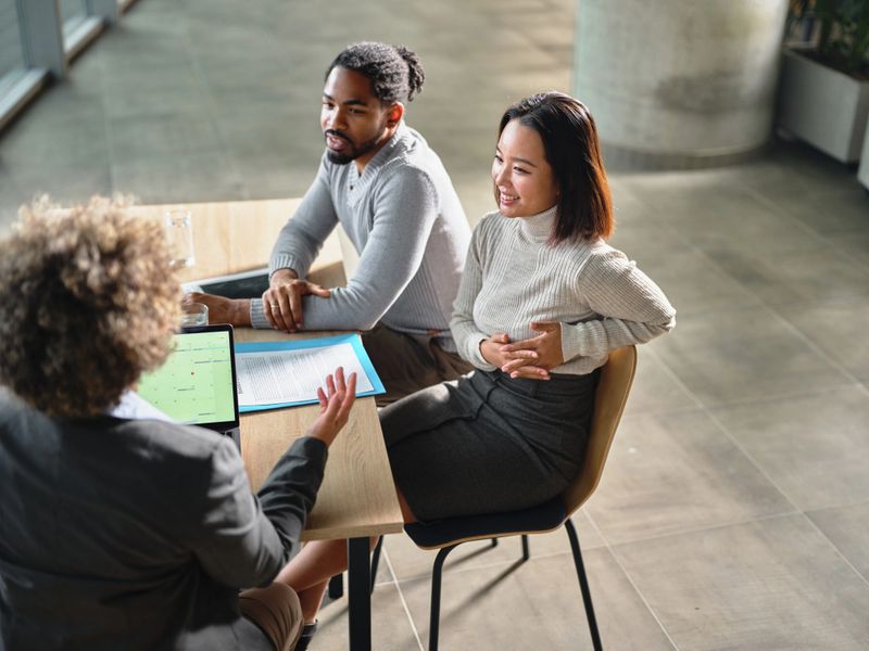 Happy diverse couple talking to their insurance agent during a meeting in the office. Focus is on Chinese woman. Photographed in medium format.