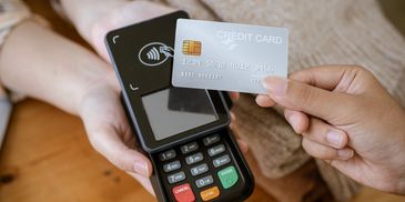 A person holds a credit card near a payment terminal for contactless payment.