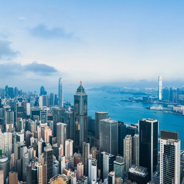 A vibrant cityscape with skyscrapers overlooking a blue harbor under a cloudy sky.