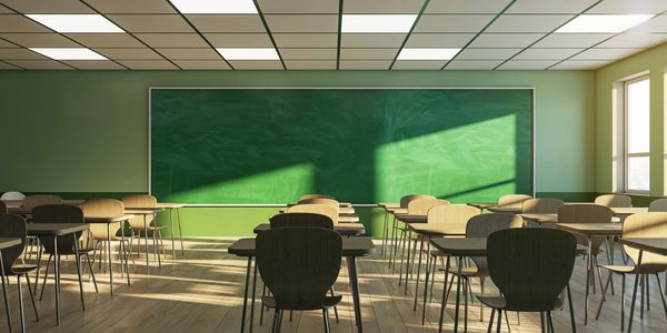 Empty classroom with sunlight streaming through windows onto desks and chalkboard.