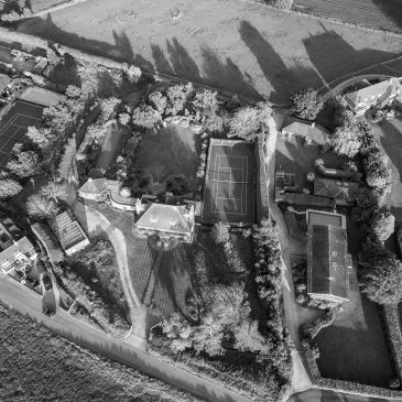 Aerial view of a residential area with tennis courts and large houses.