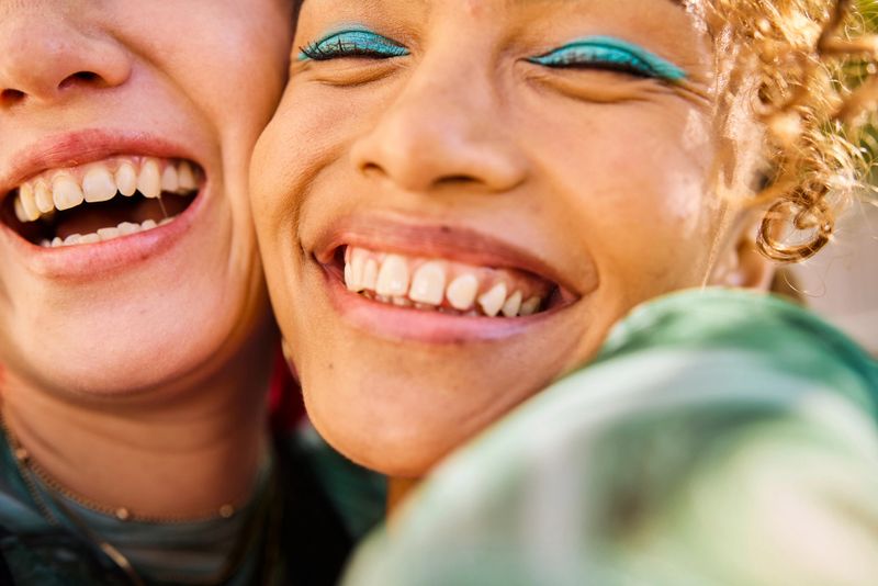 Close-up of two Gen Z adults smiling and laughing outdoors. Urban environment. Friendship and well-being.
