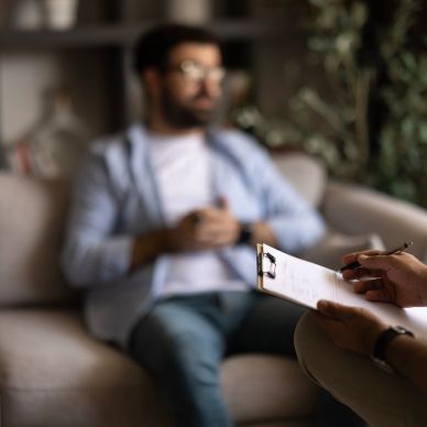Therapist taking notes while a man talks in a therapy session.