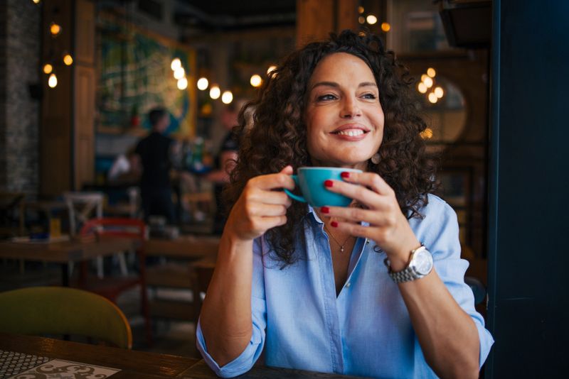 A curly hair mature woman enjoy in cafe. She drinking coffe.