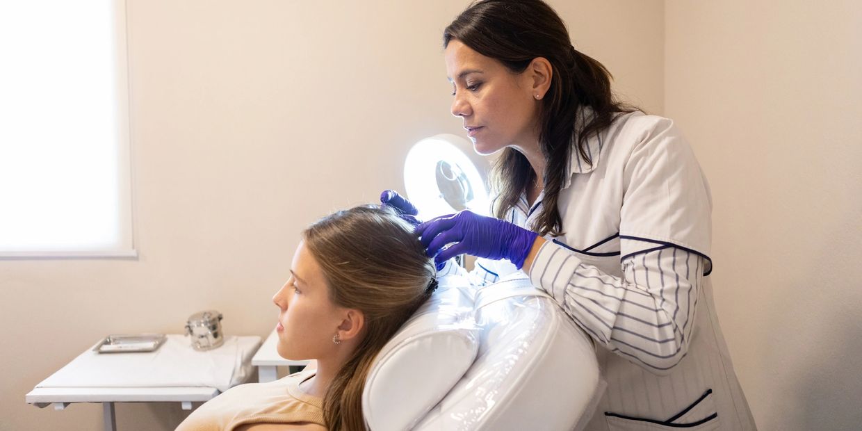 A doctor examines a patient's scalp using a magnifying lamp.