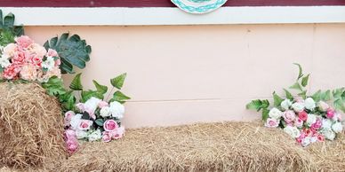 Rustic hay bale bench decorated with pink and white flower bouquets.