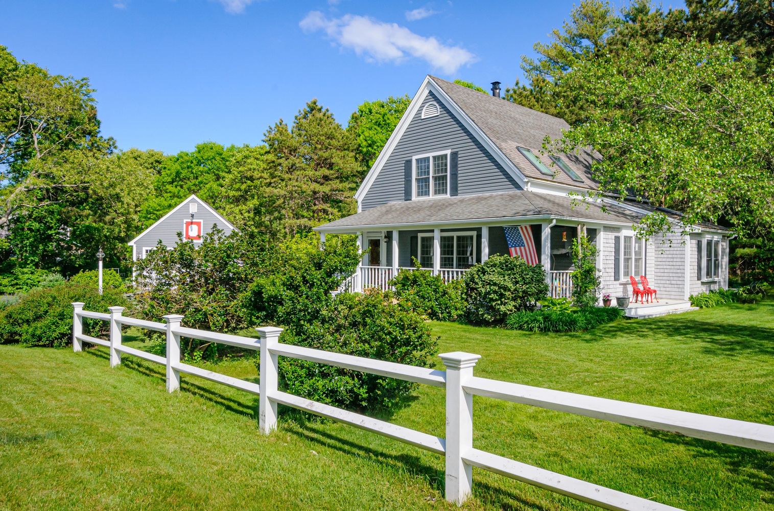 Charming gray house with white fence and lush green yard under clear blue sky.