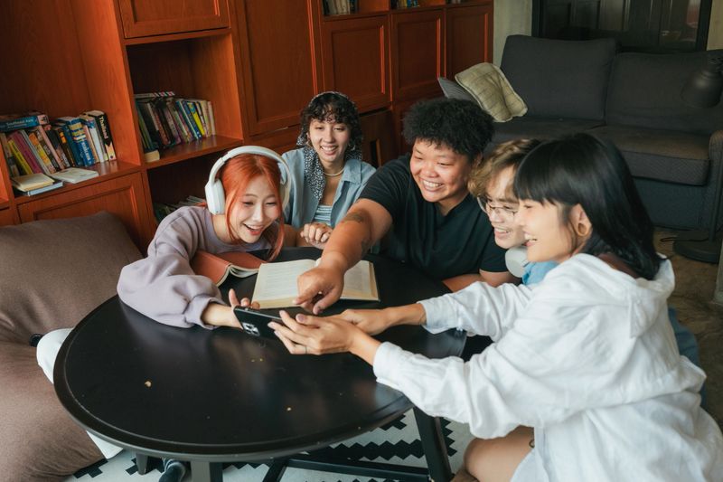 Asian guests use a smartphone to take a selfie with friends while immersed in a book, finding peace in the common area.