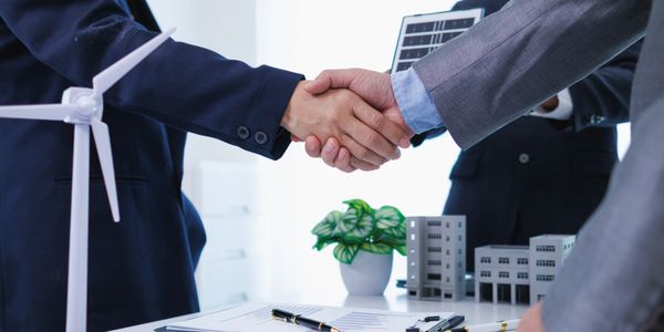 Business handshake with a model wind turbine and buildings.
