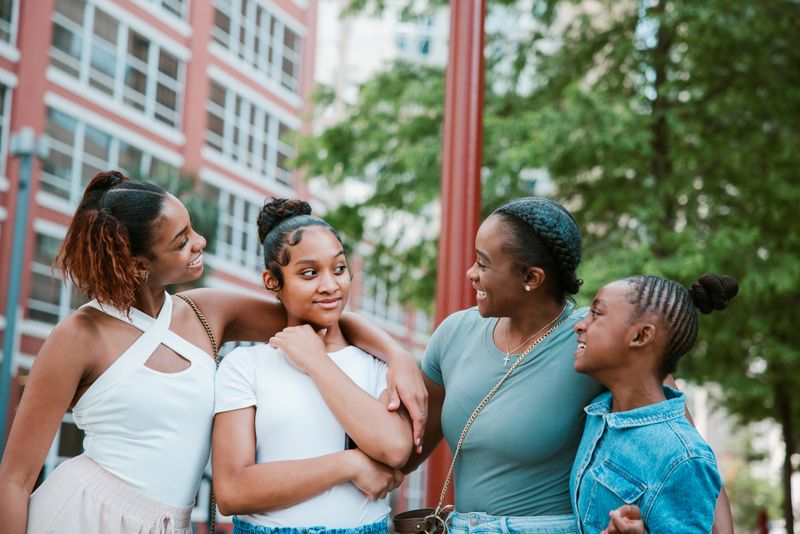 A Black mother and her daughters have fun traveling around the city of Houston, Texas.   They pause at a city corner to discuss their next plans.