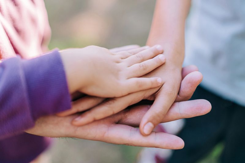 Shot of an unrecognizable family of three with their hands in a pile outdoors. Happy father and his children gathering hands in unity. Close-up shot of group of people with stacking hands.