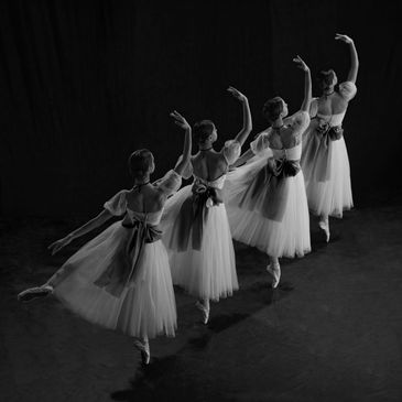 Four ballerinas dancing in a line, wearing tutus with bows.
