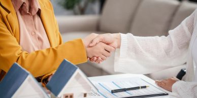 Two people shaking hands over house models and documents.