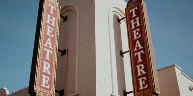 Two vintage theatre signs on a building under a clear sky.