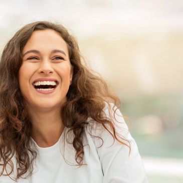 A young woman with long hair laughs while looking into the distance.