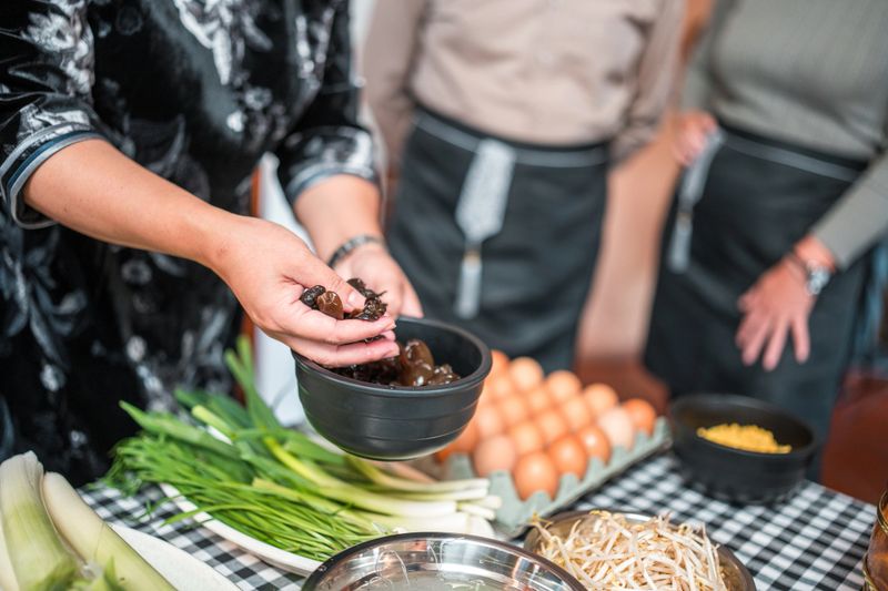 Multiracial group experience and learn the art of Chinese cuisine as they skillfully prepare ingredients for a flavorful vegetable stir-fry delight on a cooking class with beautiful Chinese female chefs.
