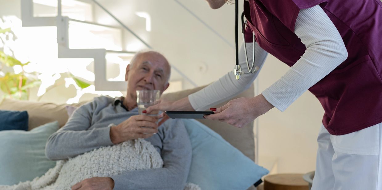 Nurse offering a tablet to an elderly man holding a glass.