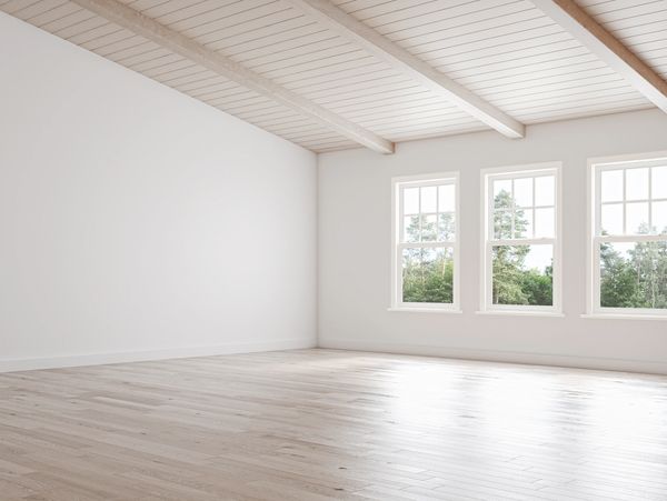 Ein leerer Raum mit hellem Holzfußboden, weißen Wänden,einer Holzbalkendecke und drei großen Fenster