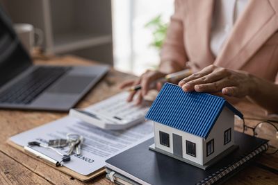 Person working on real estate paperwork with a house model and keys.