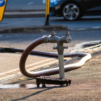 Outdoor water faucet with hose on pavement near street curb.