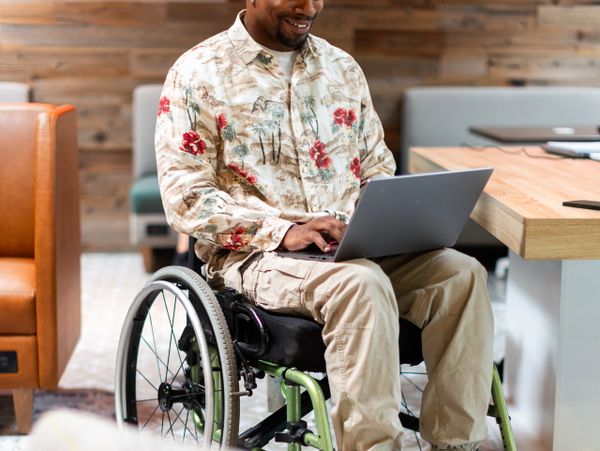 Man in a wheelchair working on a laptop, smiling.