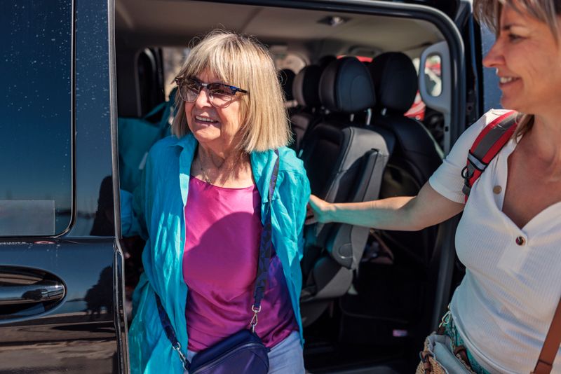 Senior woman travelling by taxi van. The woman is getting out and her mature daughter is helping her..
Shot with Canon R5