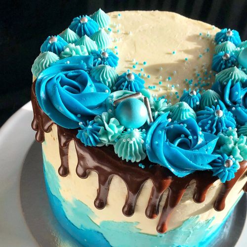 Elegant blue and white cake with chocolate drip and floral frosting.