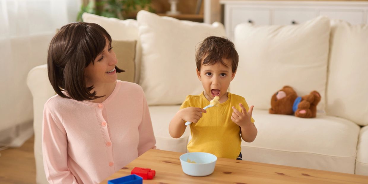 Mother watching her child eat food at home.