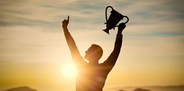 Man in front of a sunrise holding a winners cup and pointing to the sky.