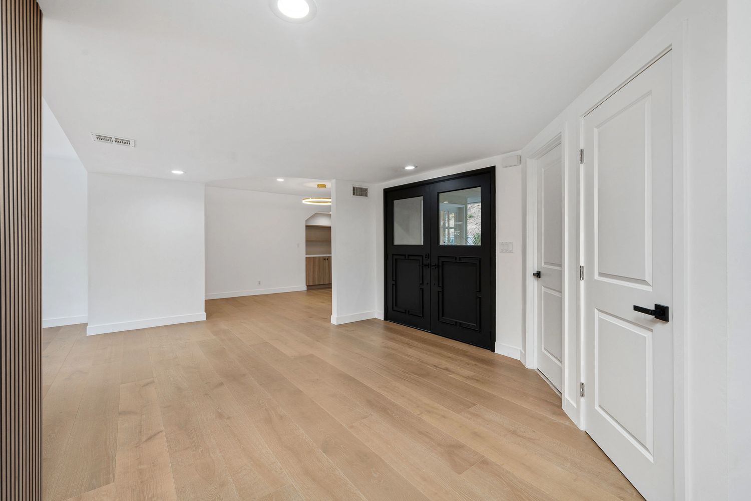 Modern entryway with black double doors and light wood flooring.