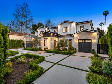 Modern two-story house with illuminated exterior and manicured landscaping at dusk.