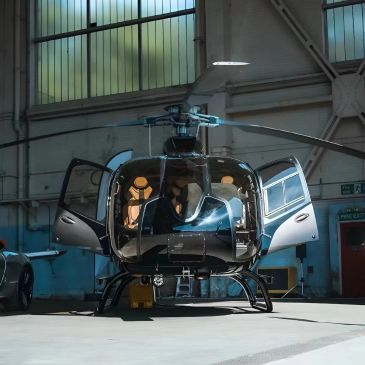 A sleek black helicopter with open doors inside a spacious hangar.