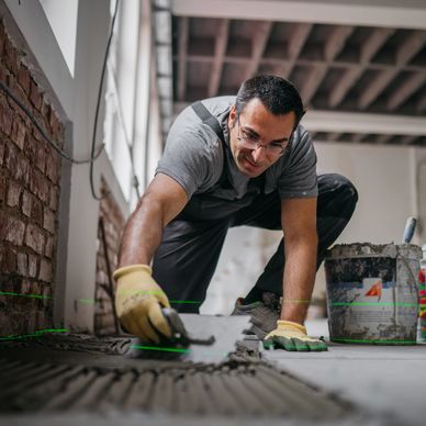 Worker laying tiles carefully using a trowel and laser level.
