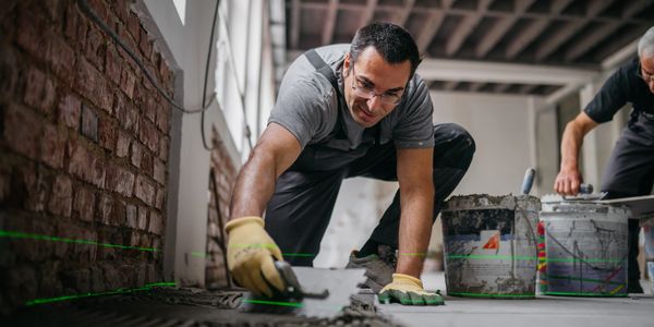 Man laying floor tiles in a room.
