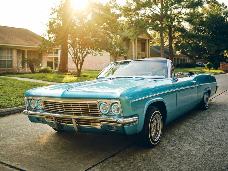 A hispanic man in his vintage lowrider convertible car, cruising on the streets in a neighborhood.