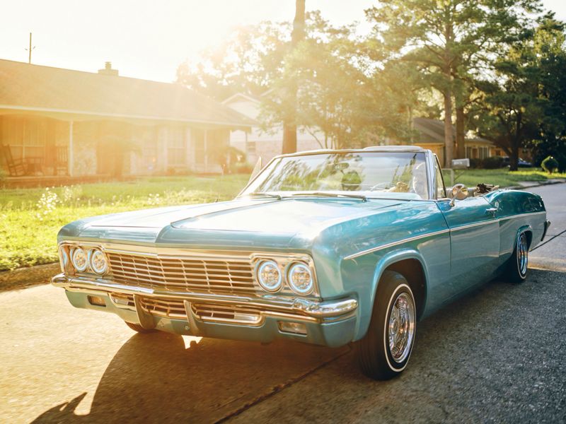 A hispanic man in his vintage lowrider convertible car, cruising on the streets in a neighborhood.