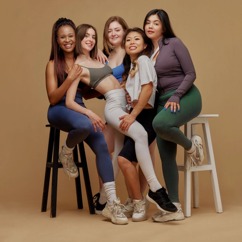 Positive, beautiful woman of different races and sizes posing together with joyful expression against beige studio background. Concept of beauty and fashion, support, unity, wellness, body positivity.