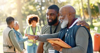 Two men outdoors, one teaching the other using a tablet.